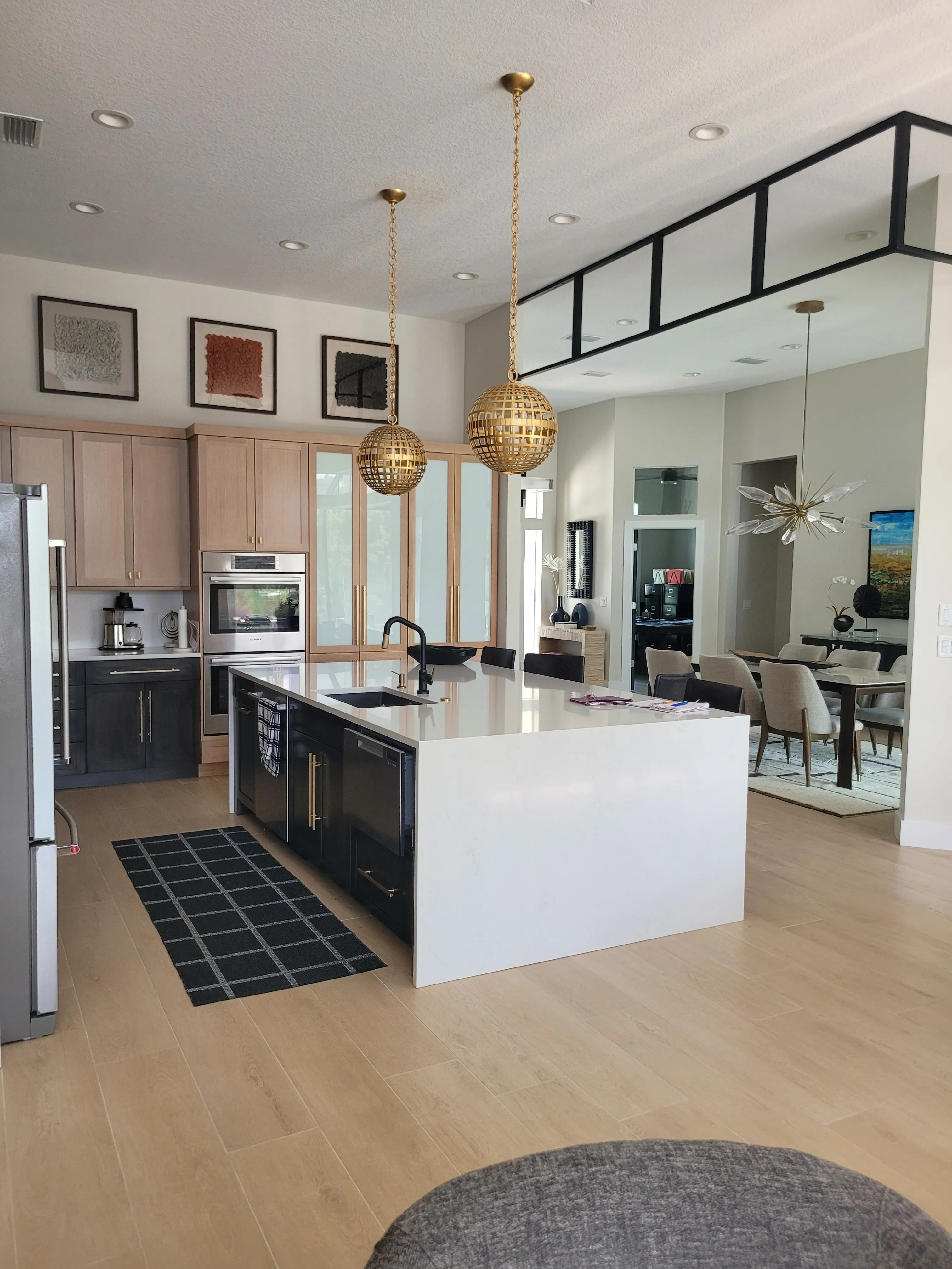 An open-plan kitchen with two-tone cabinetry, a white island and woven pendant lights